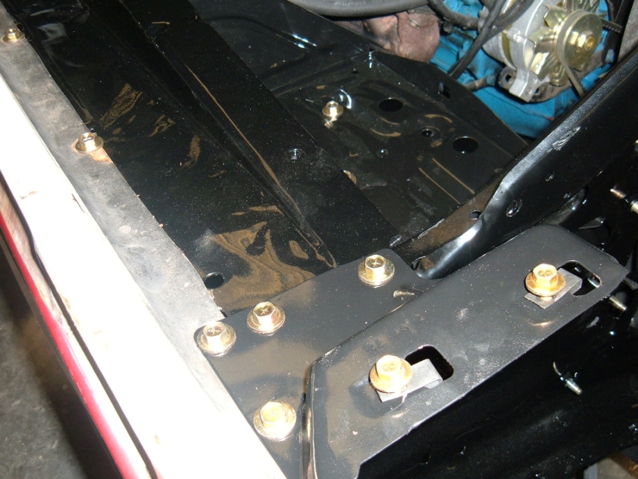 Black-painted radiator support and bracket with gold zinc bolts, engine visible in background