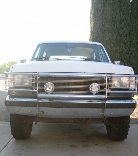1989 Ford Bronco - This white Ford Bronco, likely from the late 1980s, is presented head-on with a prominent chrome grille guard and tires.