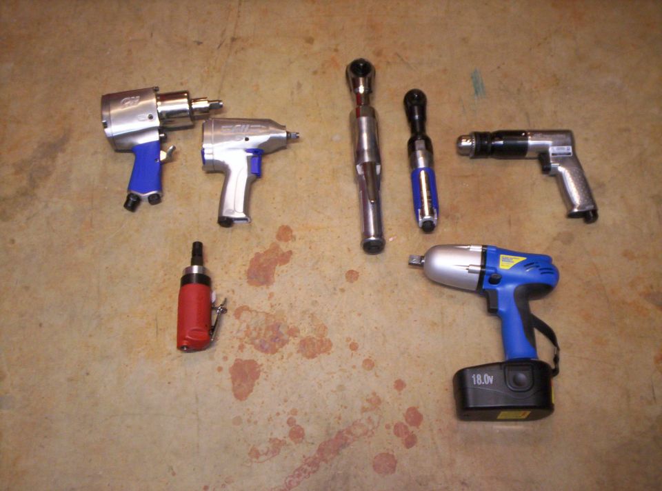 Collection of pneumatic impact wrenches, ratchets, and a drill on a concrete floor