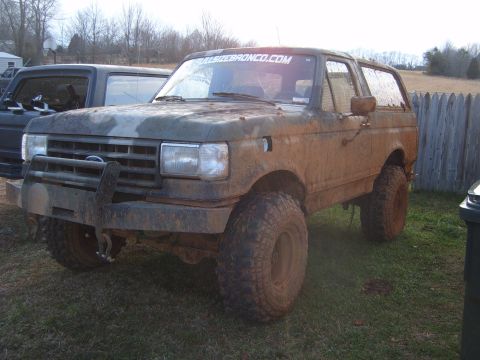 1988 Ford Bronco - This heavily muddied 1988 Ford Bronco is parked next to another dark-colored vehicle.