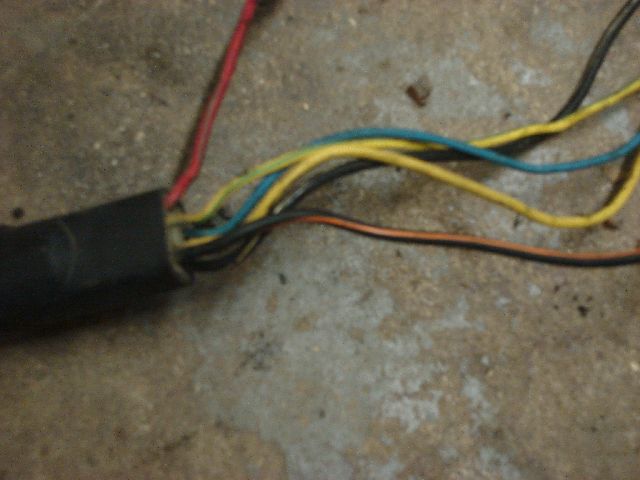 Close-up of a black automotive wiring harness with red, yellow, blue, and brown wires exposed