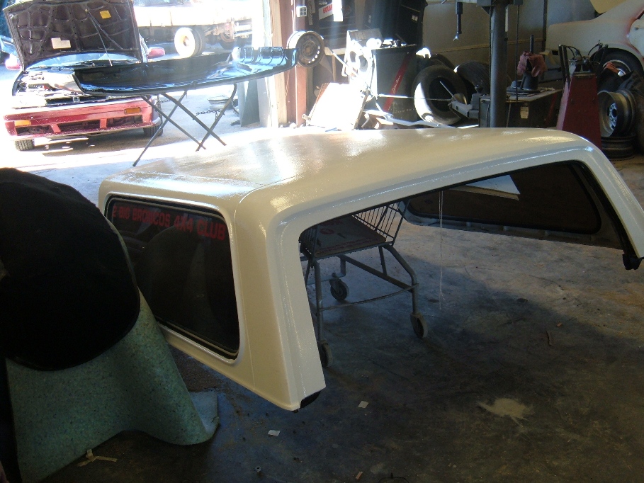 White truck cap on a cart in a garage. Red car with hood up in background