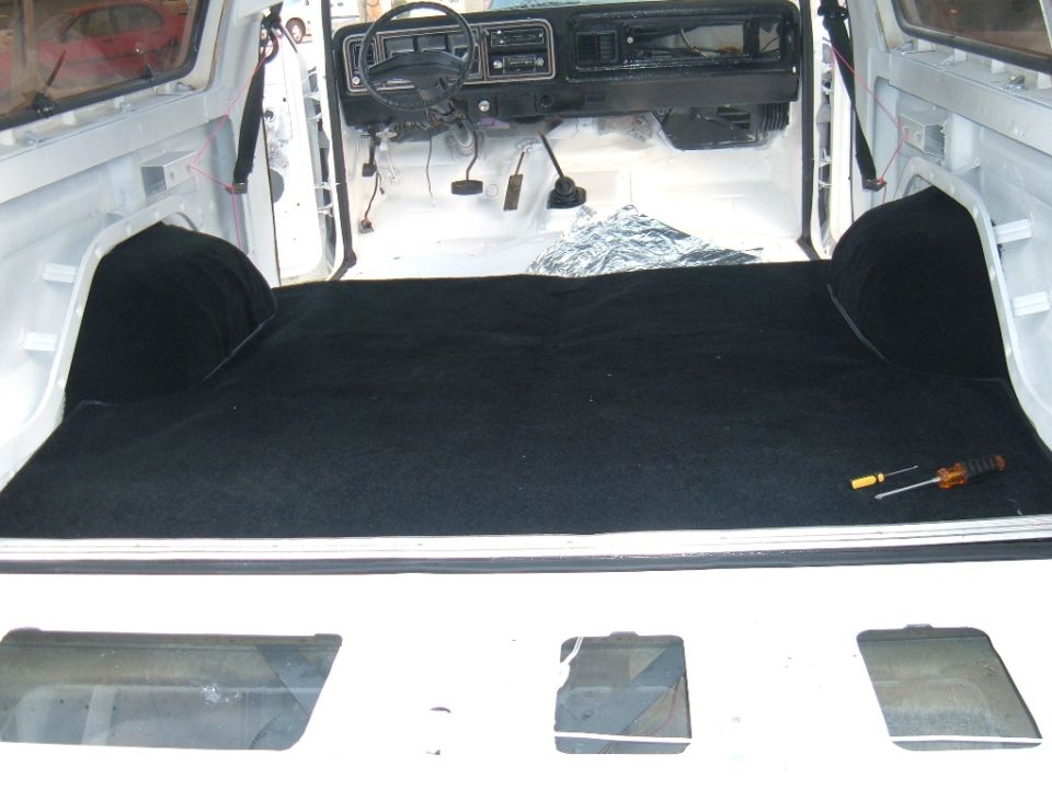 Interior of a 1978 Ford Bronco with new black carpet installed on the floor and rear cargo area. Dashboard and steering wheel are visible