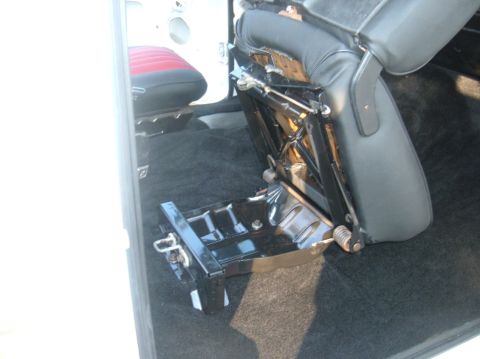 1978 Ford Bronco - The interior of a vehicle shows a removed seat base and black carpeting, with a partial view of another seat.