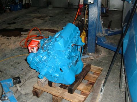 1978 Ford Bronco - A bright blue engine and transmission assembly sits on a wooden pallet in a garage, with a blue vehicle partially visible on the right.