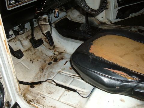 1978 Ford Bronco - The interior of a vehicle shows a worn driver's seat and dirty floor with pedals visible.