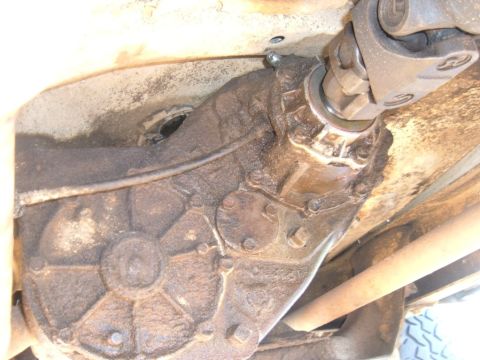 1978 Ford Bronco - The transfer case and driveshaft are visible from underneath the vehicle, coated in grime.
