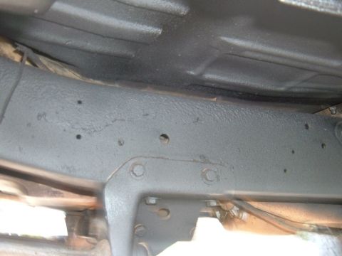 1978 Ford Bronco - The undercarriage of a vehicle shows a frame coated in black material, with visible bolts and some wiring.