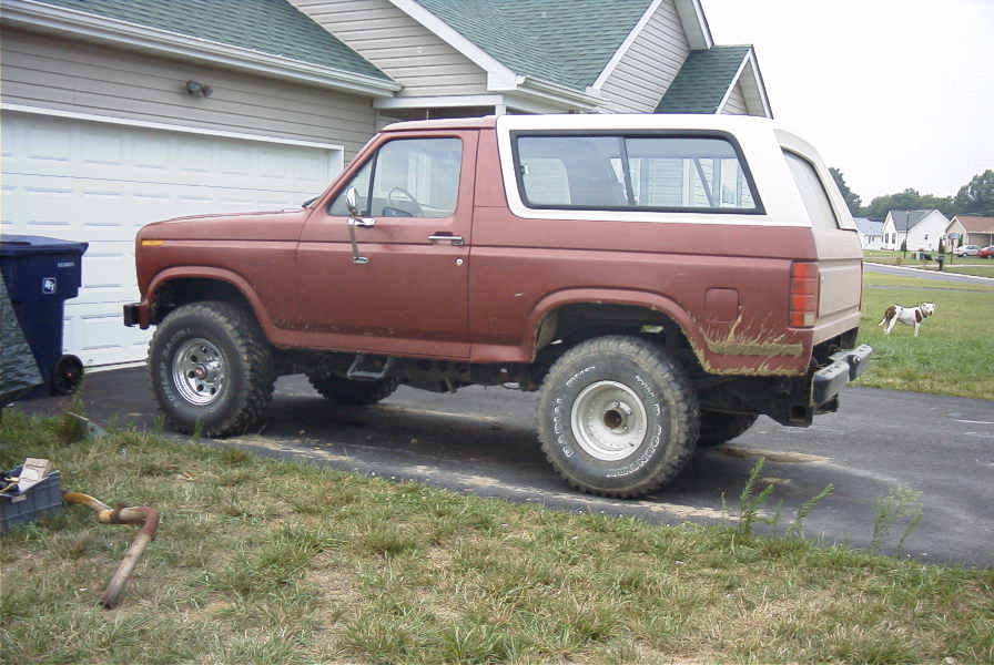 Lifted brown and white Ford Bronco SUV on mud tires parked in a driveway