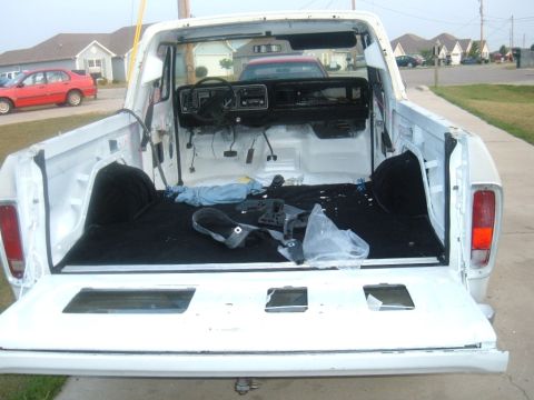 1978 Ford Bronco - Rear view of a disassembled pickup truck's interior and bed, with a red car in the background.