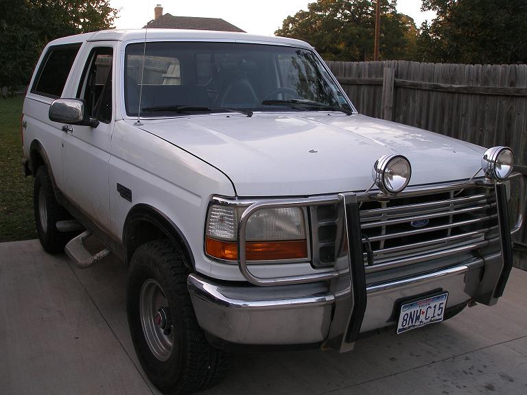 White Ford Bronco SUV with chrome brush guard and round lights, front 3/4 view on driveway