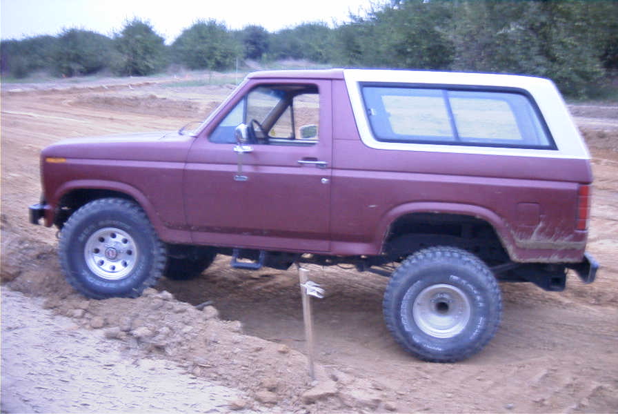 Side profile of a lifted maroon Ford Bronco with white hardtop on a dirt off-road course