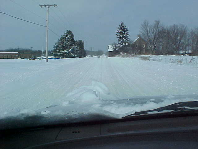 Snow-covered rural road seen through a vehicle windshield