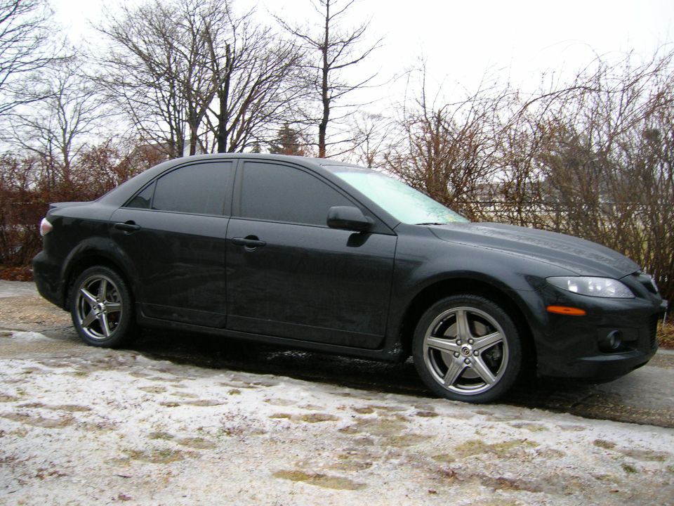Black sedan parked on a snowy surface, side view with front quarter angle