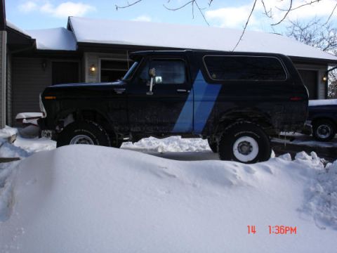 1979 Ford Bronco - A black 1979 Ford Bronco with a blue stripe is parked in the snow, partially obscured by a snowdrift.