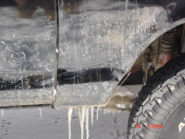Ice-covered dark quarter panel and door with icicles, red shock and all-terrain tire visible in wheel well