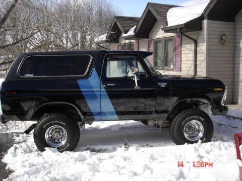 1979 Ford Bronco - Side view of a black 1978 Ford Bronco with a blue stripe, parked in the snow outside a house.