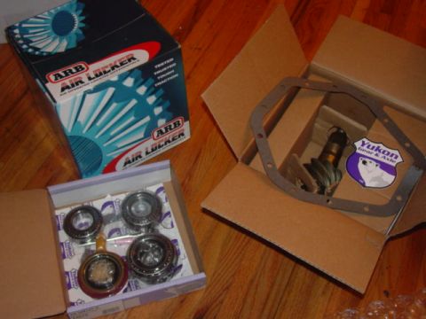 1986 Ford Bronco - Automotive parts including an ARB Air Locker box and Yukon differential components are laid out on a wooden surface.