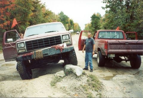 1980 Ford Bronco - Two red Ford trucks, an SUV and a pickup, are parked on a dirt road with a man standing between them.