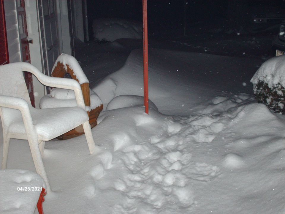 Plastic chairs and a planter covered in snow, with a red pole in the middle. Date stamp 04/25/2021