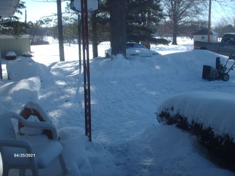 1995 Ford Probe - A white car is almost completely covered in snow, with a pickup truck visible in the distance.