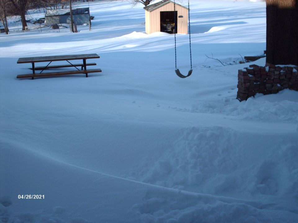 Snow-covered yard with picnic table, shed, and swing set. Date stamp 04/26/2021