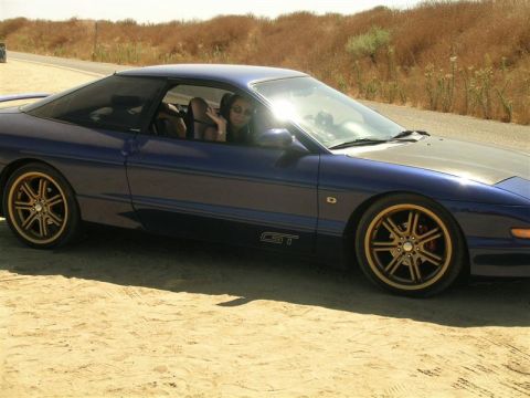 1994 Ford Probe - A blue 1994 Ford Probe GT with gold rims is seen from the side on a dirt road.