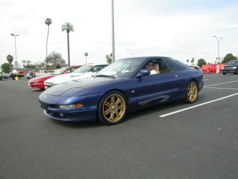 1994 Ford Probe - A blue 1994 Ford Probe GT is parked in a lot with other vehicles around it.
