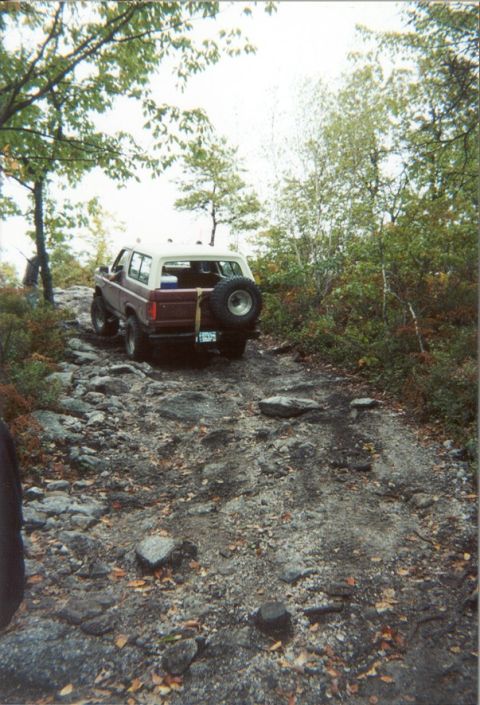 1980 Ford Bronco - This 1980 Ford Bronco navigates a challenging, rocky off-road path surrounded by trees.