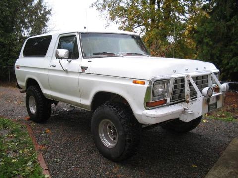 1979 Ford Bronco - A white 1978 Ford Bronco is shown from a 3/4 front angle, parked on a gravel surface with trees in the background.
