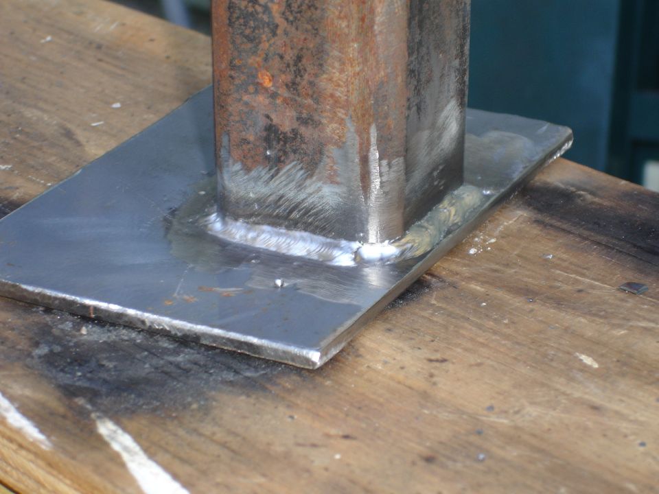 Welded metal bracket on wooden surface. Visible Supermotors.net logo