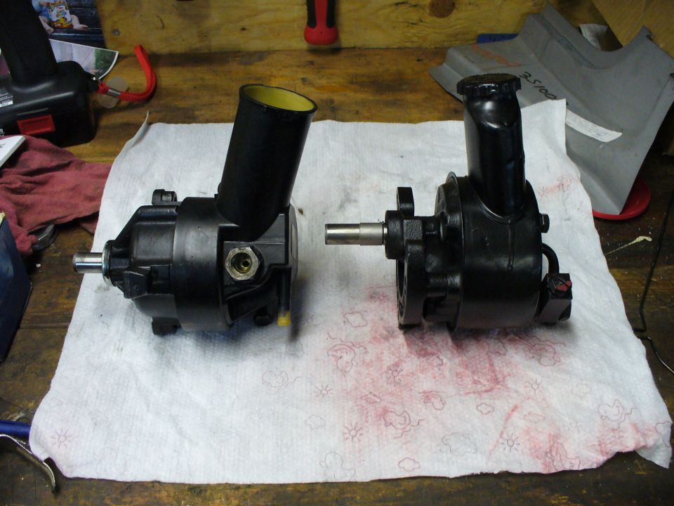 Two black power steering pumps with reservoirs side by side on a towel on a workbench