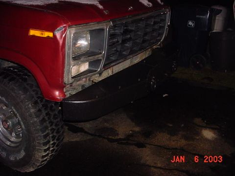 1980 Ford Bronco - Front corner of a red pickup truck with a black bumper and a prominent grille is shown.