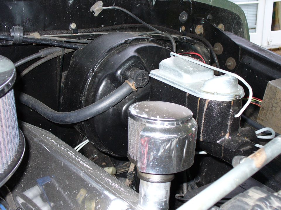Brake booster and master cylinder assembly in a vehicle engine bay, with chrome air cleaner visible