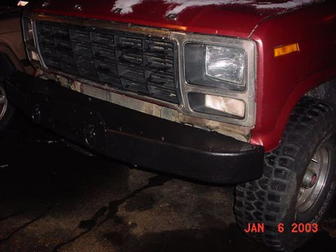 1980 Ford Bronco - Front view of a red truck with a black bumper and a prominent chrome grille, showing a portion of the headlight and turn signal.