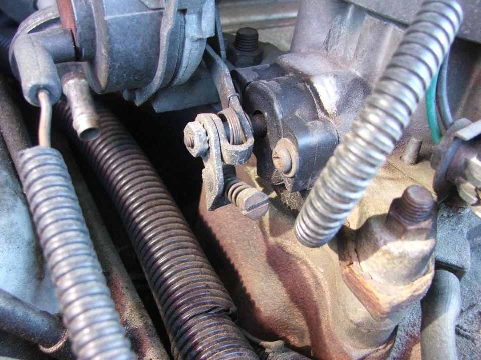 Close-up of throttle linkage bracket and cable on a corroded engine bay component