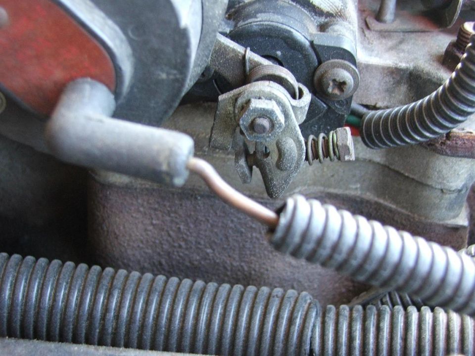 Macro shot of throttle linkage arm, spring cam and copper wire in an engine bay