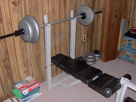 1996 Chevrolet Cavalier - A weight bench setup with a barbell loaded with weights is shown in a room with wood-paneled walls.