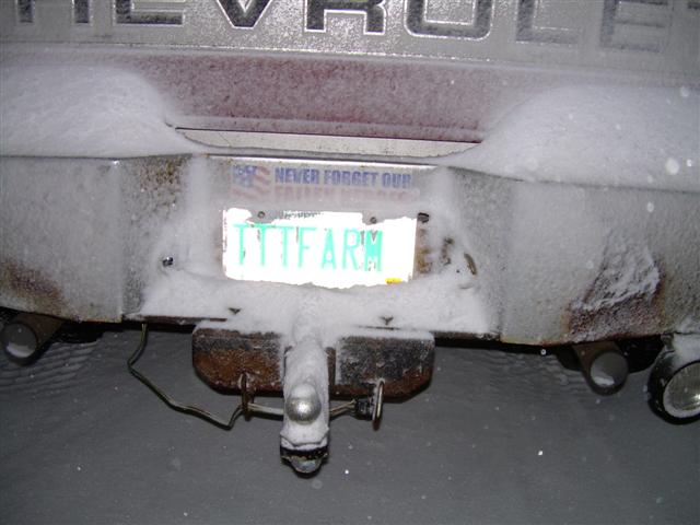 Rear bumper of a Chevrolet truck covered in snow, with a license plate reading 'TYT FARM'