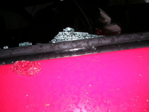 1996 Ford Probe - Shattered window glass litters the top of a pink car door, with a large piece of glass resting on the door's surface.