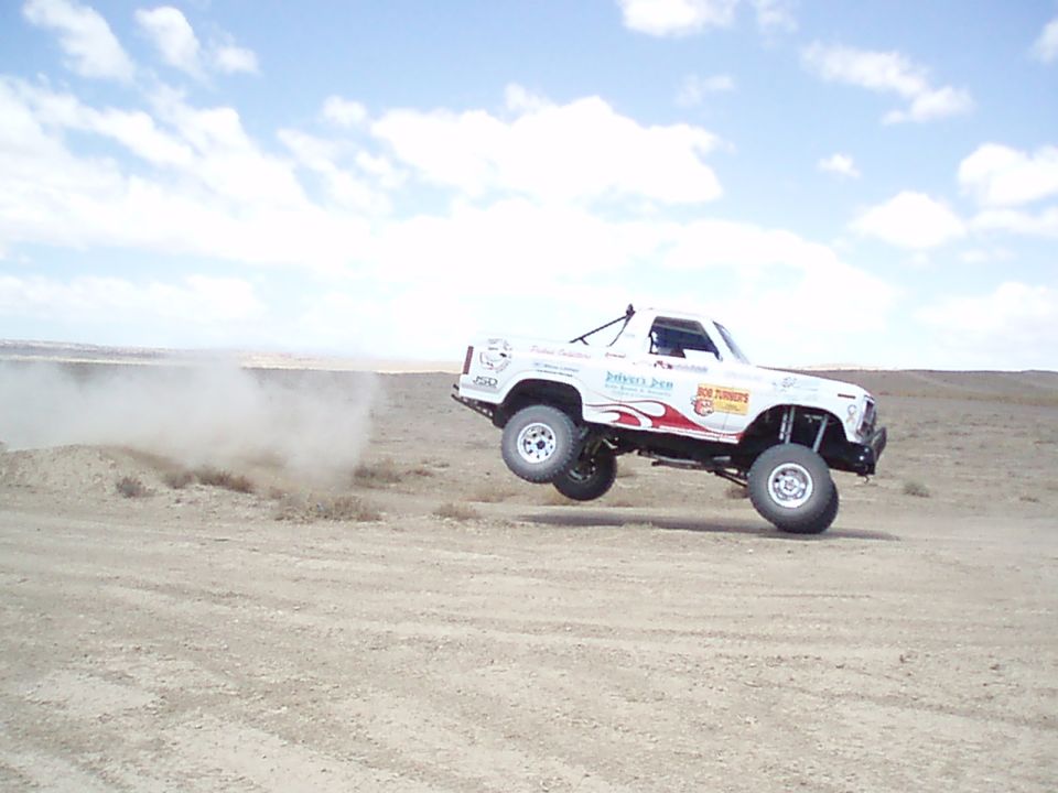 White off-road race truck jumping over a desert dirt berm under blue sky