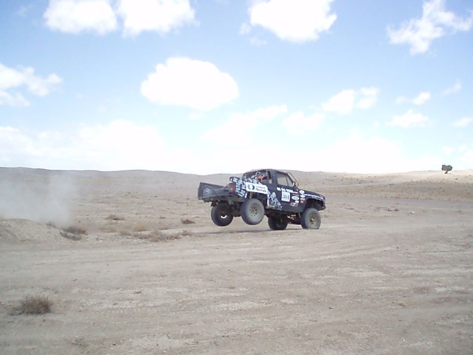 Dark off-road race truck jumping in the desert with dust trailing behind