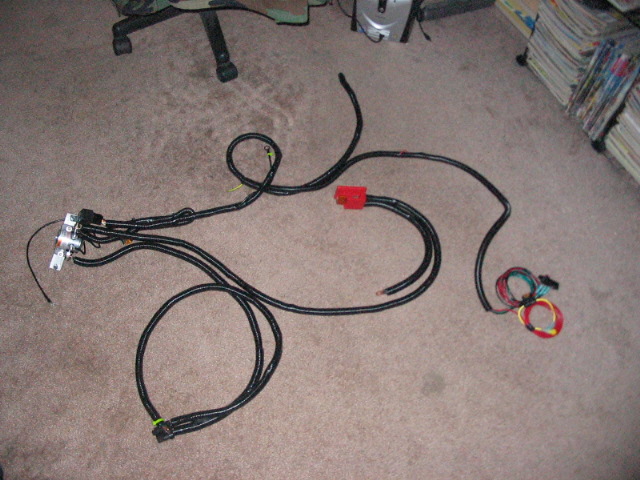 Wiring harness with red connector and multiple black cables spread on carpet