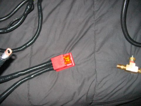 1991 Ford Bronco - Automotive wiring harness components, including a red connector and a brass T-fitting, against a dark fabric background.