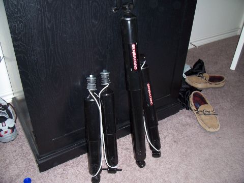 2003 Ford Ranger - Four SENSATRAC shock absorbers are displayed indoors, with shoes and a sneaker visible in the background.