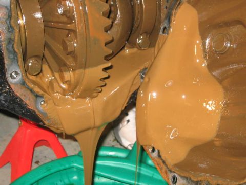 1979 Ford Bronco - The image shows a close-up of a vehicle's differential with thick, brown fluid draining out into a green collection pan.
