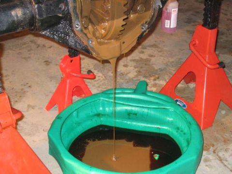 1979 Ford Bronco - Differential fluid being drained into a catch pan with vehicle supported by jack stands.