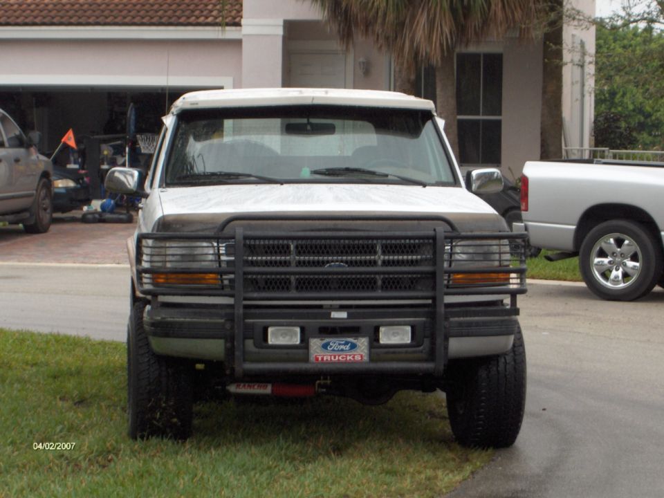 White Ford SUV with black brush guard and lift, parked in driveway, front view
