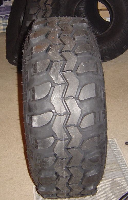 Tread close-up of a used mud-terrain off-road tire standing on carpet indoors