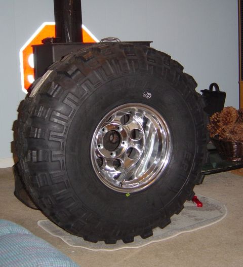 1986 Ford Bronco - A mud-terrain tire lettered "SUPER" (Super Swamper style) mounted on a polished eight-hole aluminum wheel, standing indoors on carpet in fr…